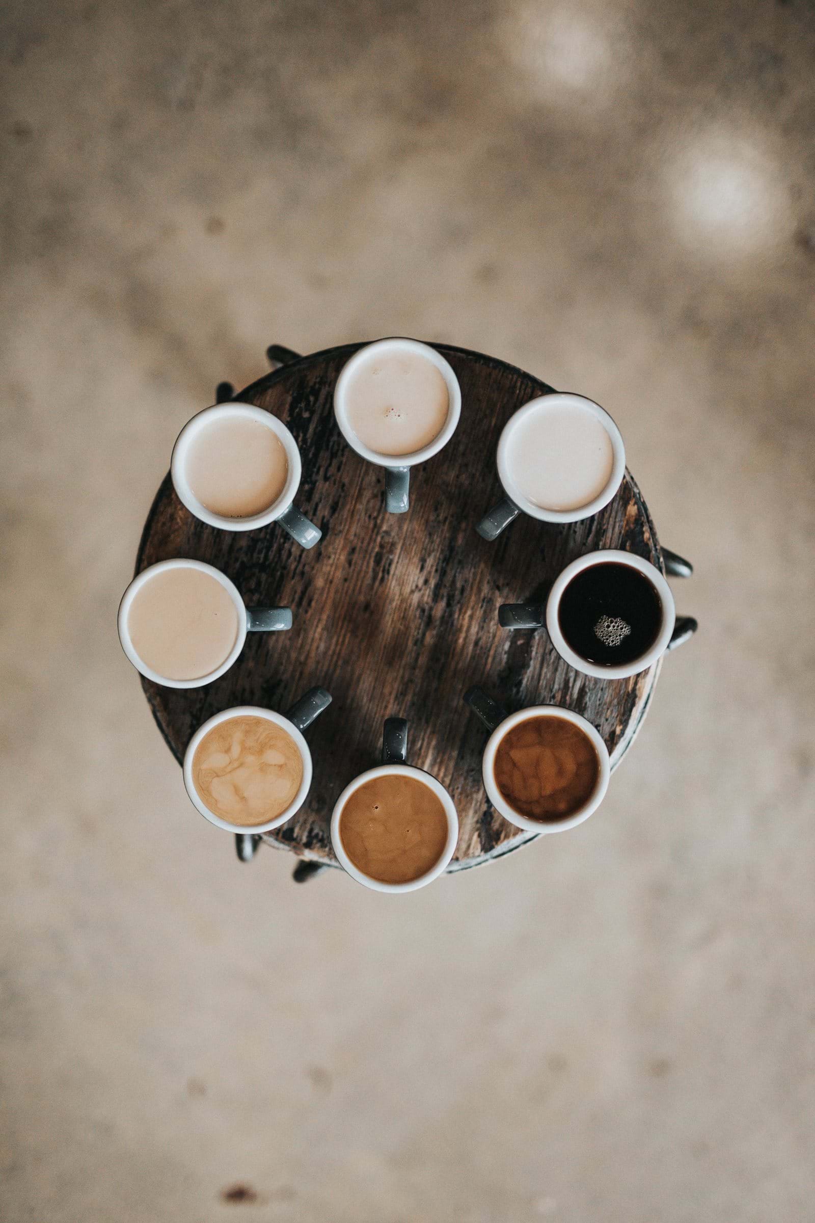 Åtta kaffekoppar med olika mjölkmängd stående på ett bord av trä
