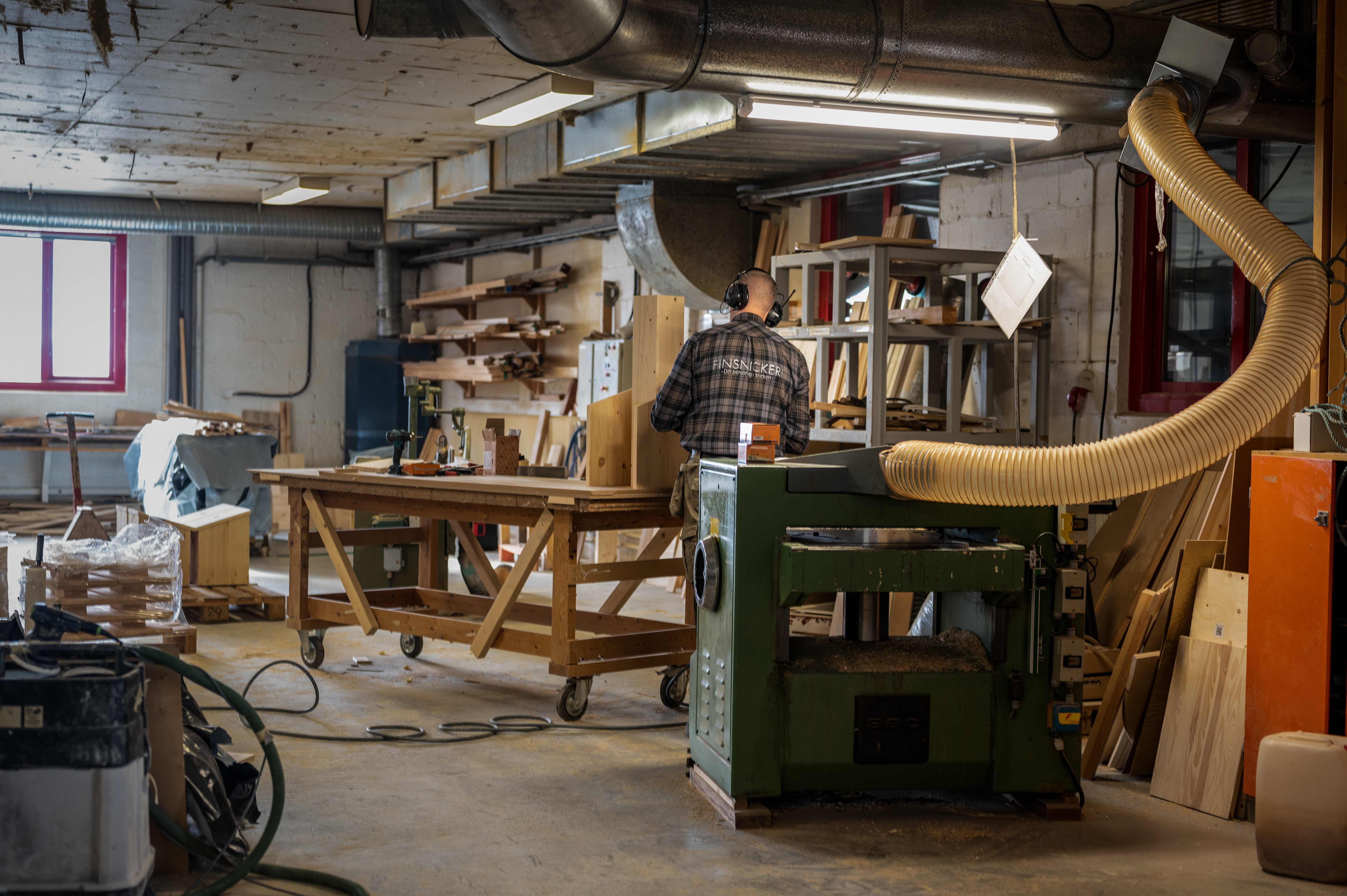 Germund med ryggen mot kameran står och jobbar i snickeriet bakom planhyveln